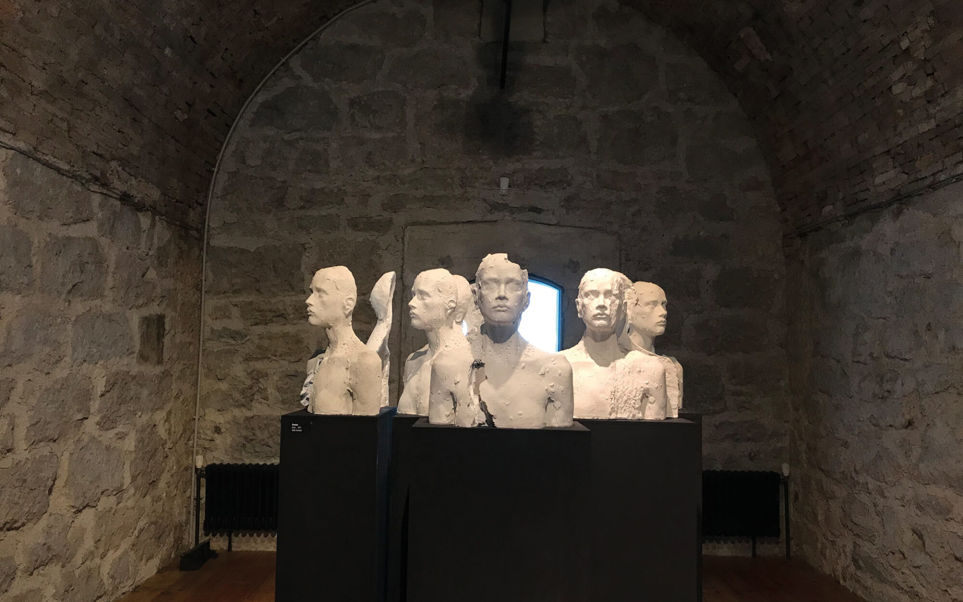 vista frontale dell'opera -Domino-, della scultrice trentina Laura Marcolini, esposta in occasione della mostra Fragile, presso il Forte superiore di Nago, nel 2021. Tredici elementi in gesso su colonne grigie.